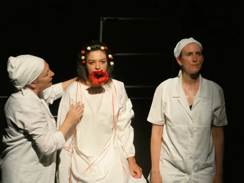 Three performers: one crowned with flowers and red-mouthed, flanked by two in white