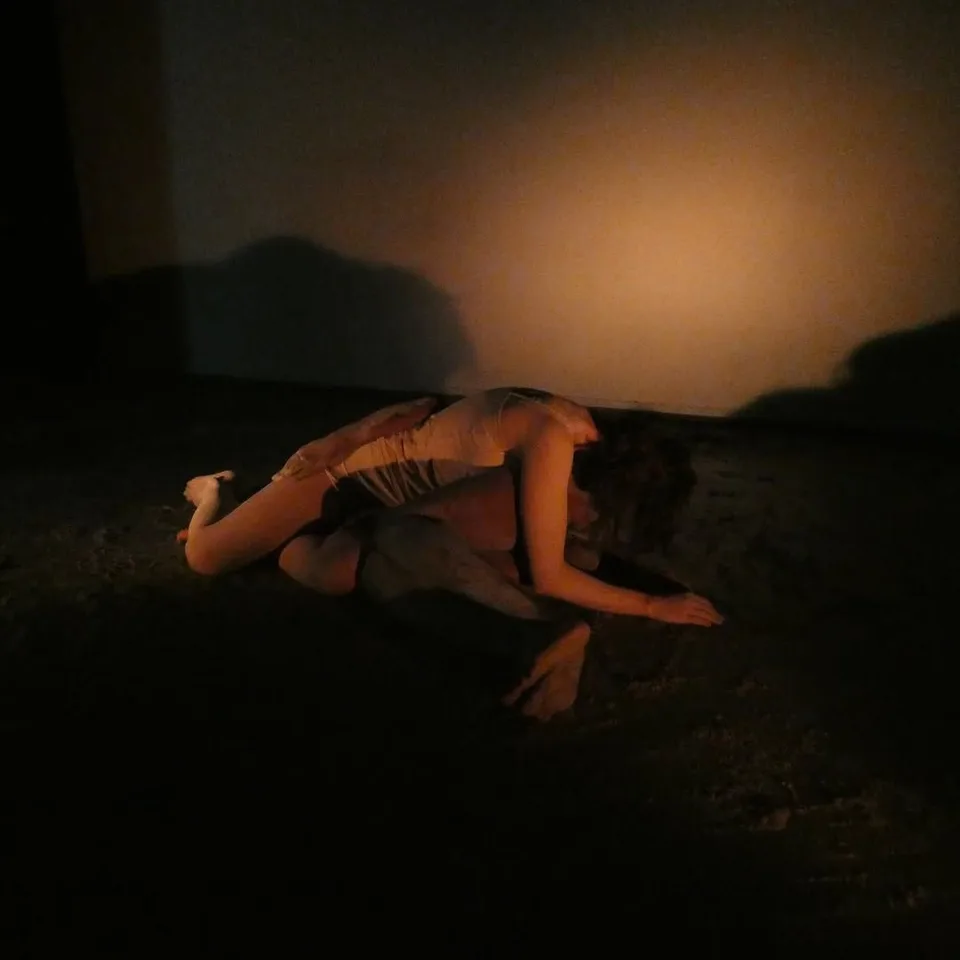 Two performers low on the floor in warm light