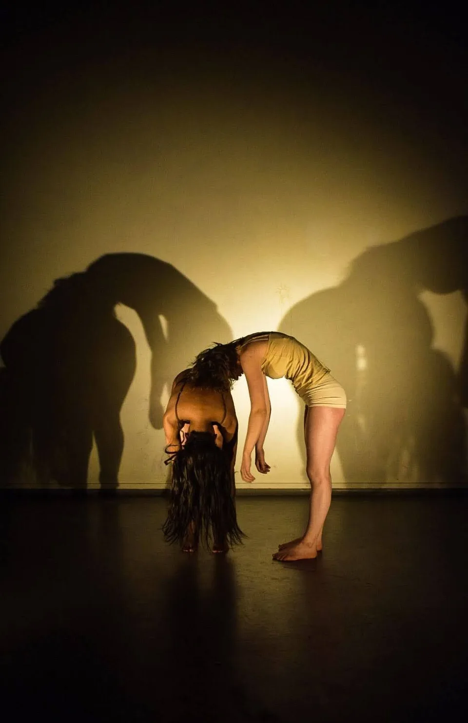 A performer bent forward with hair hanging down, huge shadows behind them