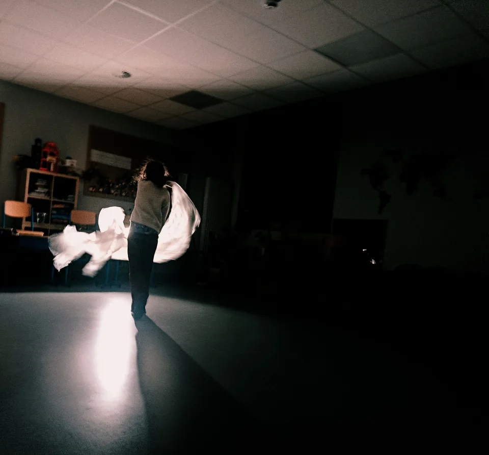 Two people in white lit by a single beam across a dark studio floor