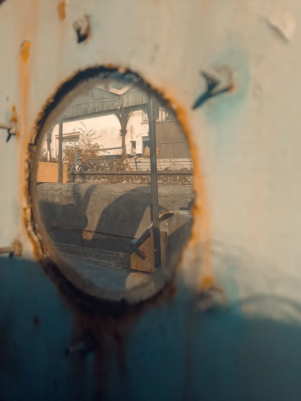 A round, rust-spotted mirror on a wall, reflecting a covered walkway