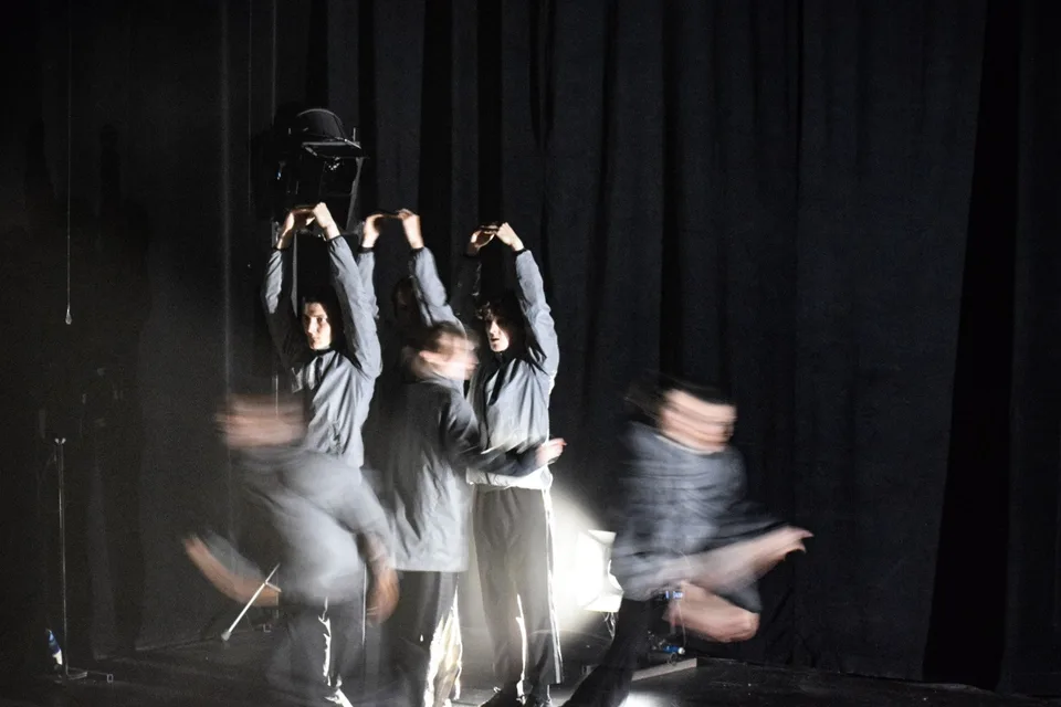 Performers blurred with motion in front of a dark curtain