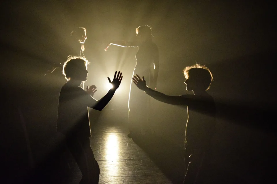 Silhouetted figures in a corridor of golden haze, hands raised into the light — from Tip of the Tongue