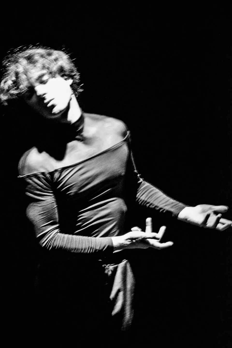Black-and-white: a performer with bare shoulders, hands curled in front of them