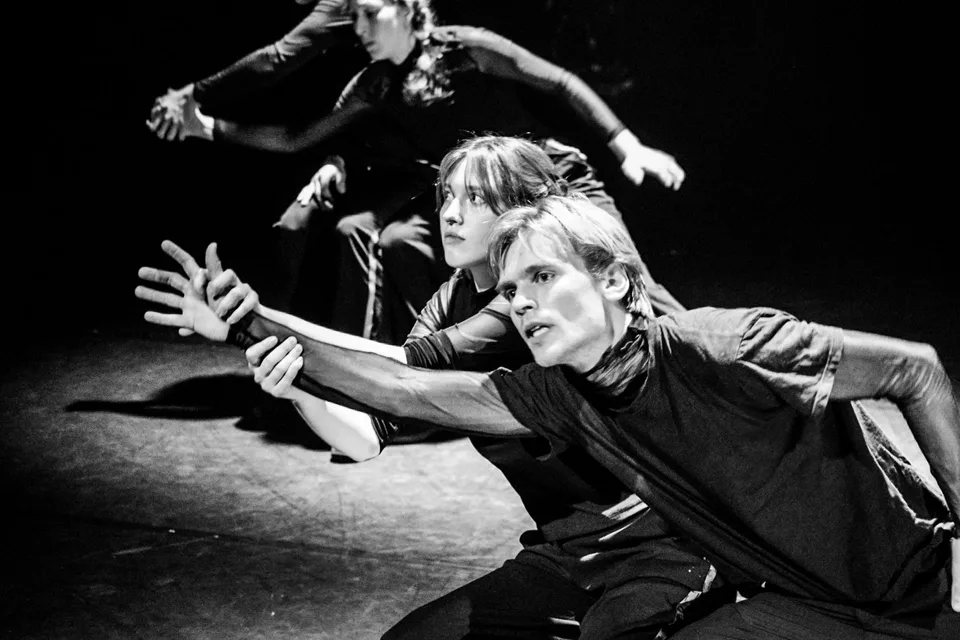Black-and-white: two performers low to the ground, arms stretched out