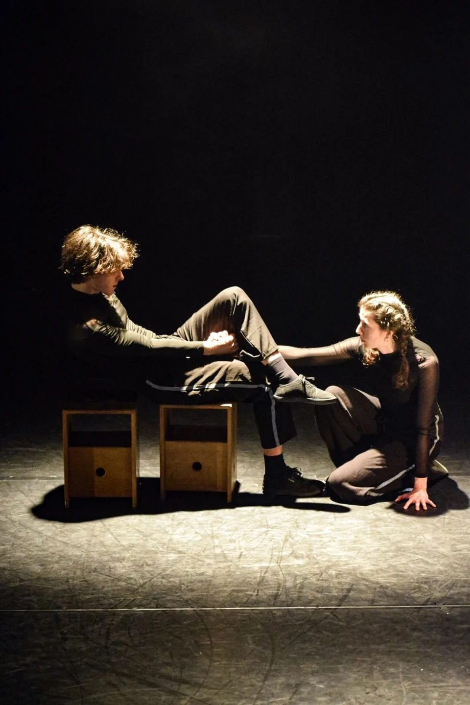 Two performers seated on a pale floor with small wooden boxes between them