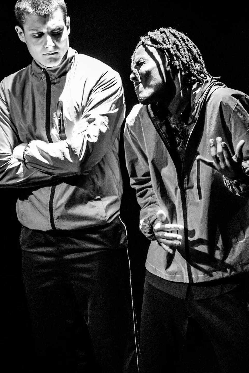 Black-and-white: two performers standing face to face, arms folded