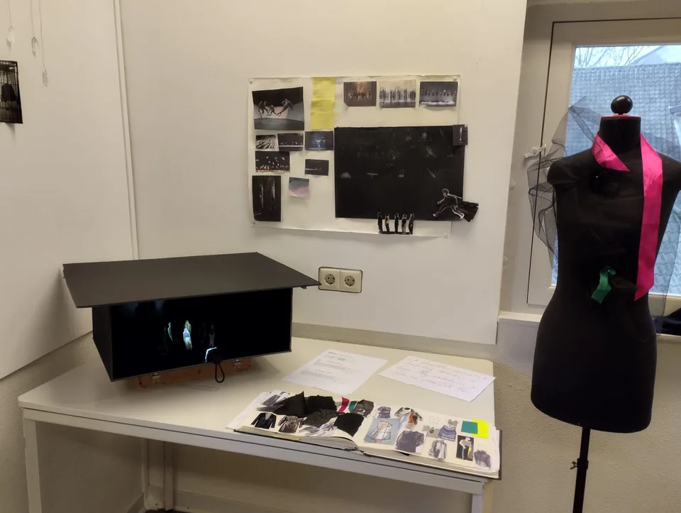 A workroom table with a black scale-model box, a dress form and printed references