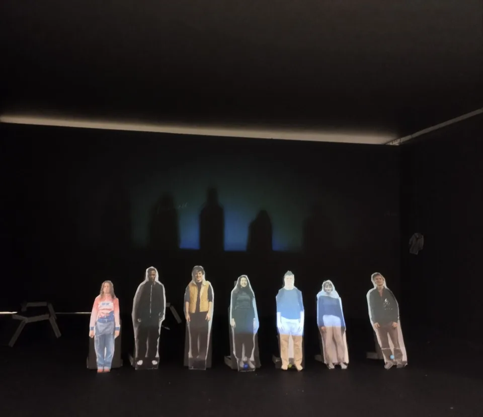 Seven small paper figures standing in a row inside the lit scale model
