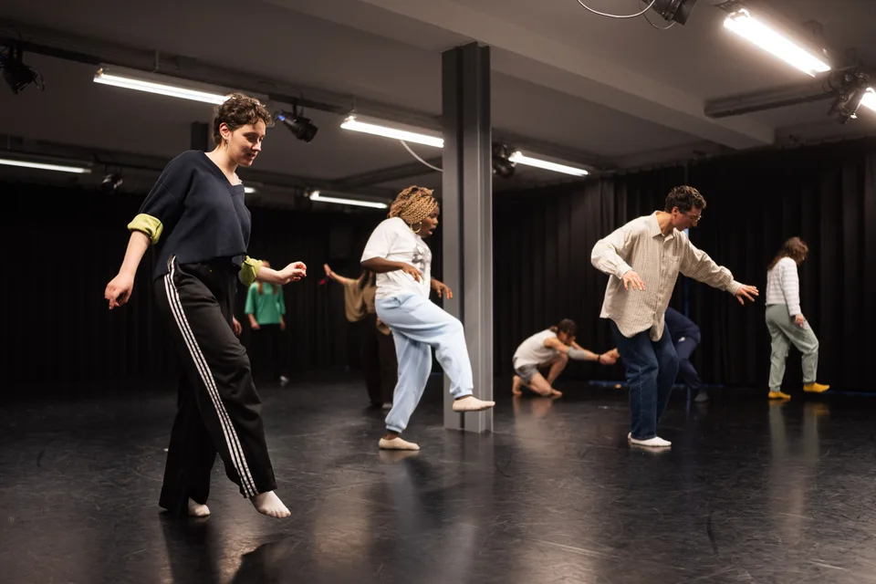 A participant stepping wide across the studio, others scattered behind